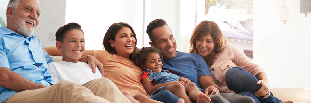 Multi-Generation Hispanic Family Relaxing At Home Sitting On Sofa Watching TV Together
