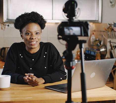 Happy smiling young beautiful black vlogger woman filming new video using professional camera at home table slow motion  Creative blogging and vlogging as a modern freelance work and profession 